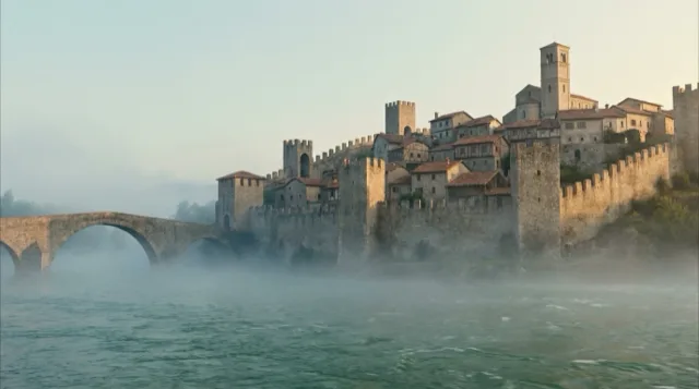 A walled hill town at dawn around the year 1000: mist off the river, smoke from the roofs.