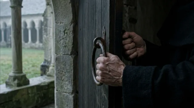 Weathered hands on the iron ring of a heavy oak door, closing it.