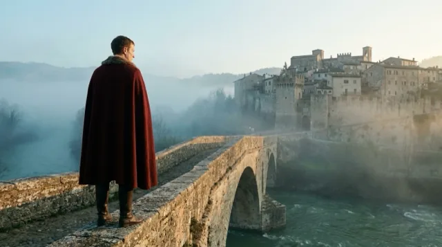 The lord of Ivrea from behind at the bridge's parapet, facing the town at dawn.