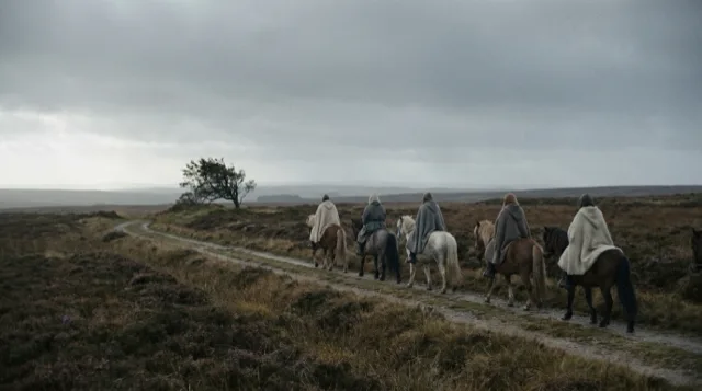A file of riders crosses an open heath under a low grey sky, seen from far off.