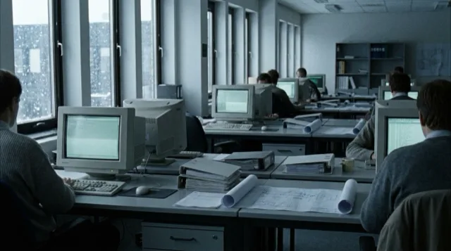 An early-1990s engineering office on a winter afternoon: rows of desks, boxy monitors, snow outside.