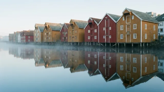 A row of wooden wharf warehouses on a Norwegian river at dawn.