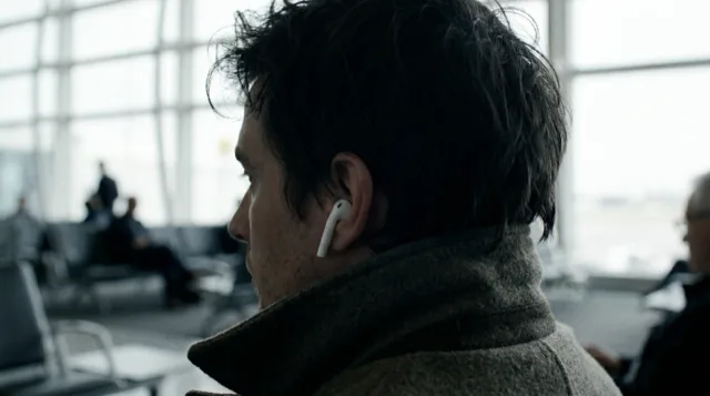 Close from behind on a traveller's ear with a small white earbud.
