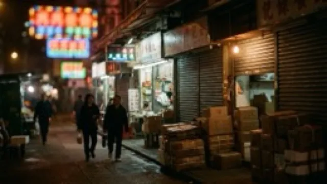 A narrow street of small electronics shopfronts at night, all signs soft as coloured light.