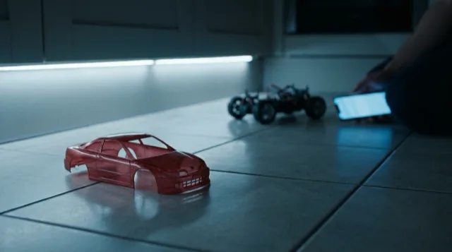 The empty red shell on the tiles, the chassis and the phone's glow soft behind.
